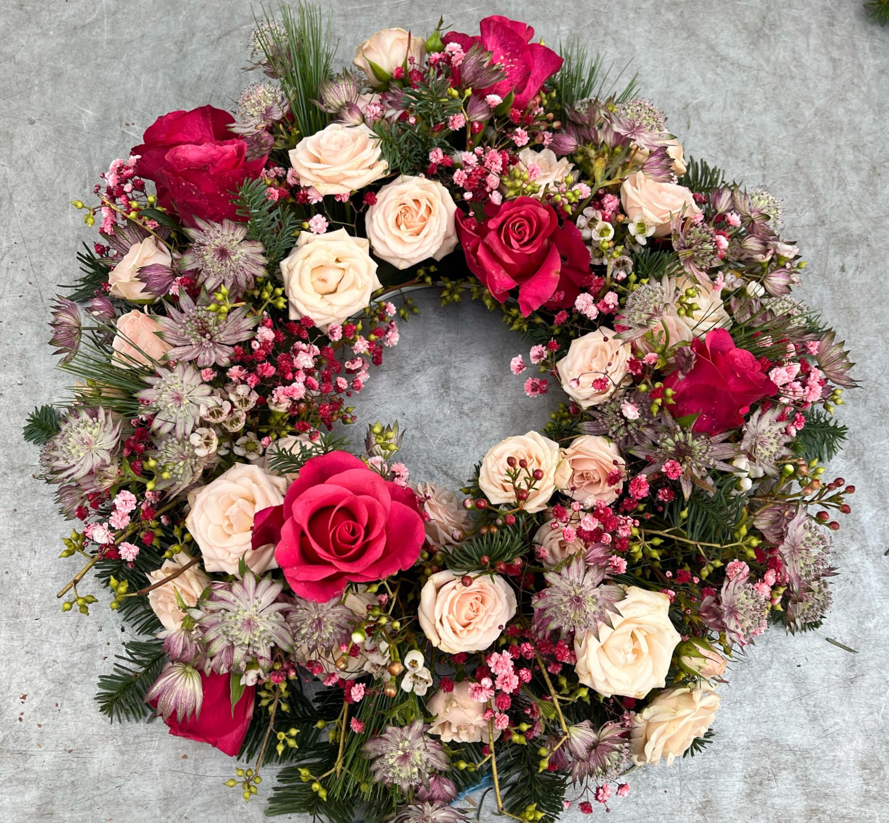 Trauerkranz aus magentafarbenen und cremefarbenen Rosen mit Sterndolden und Tannengrün