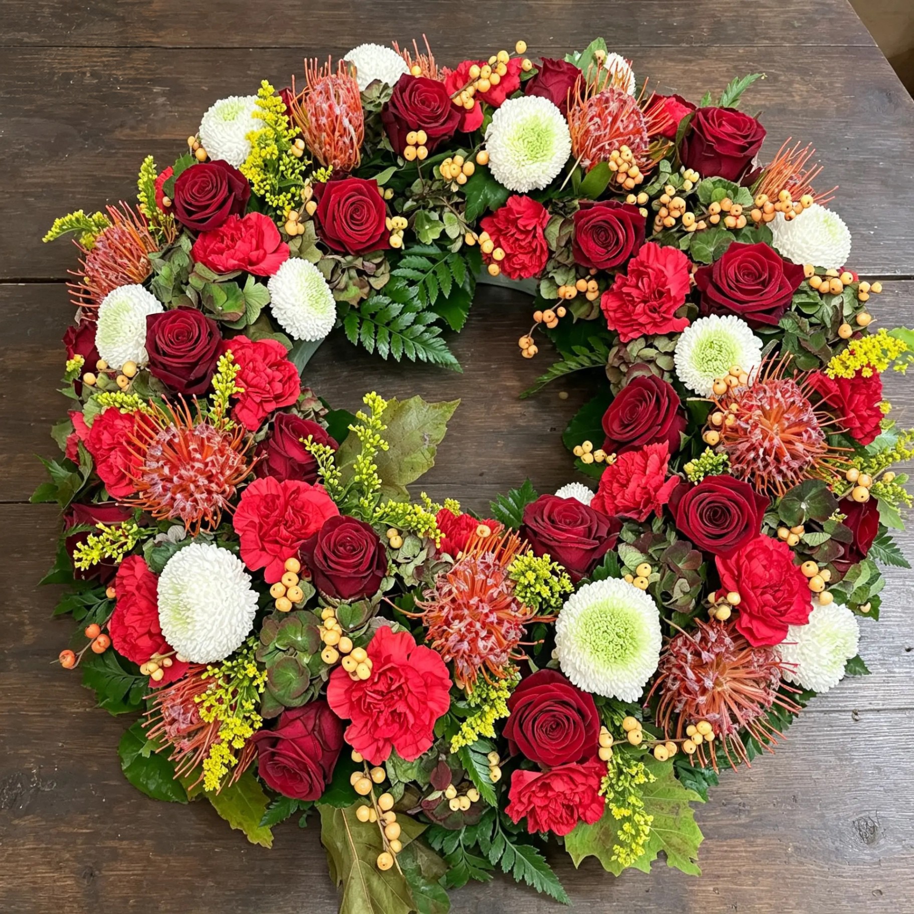 Bunter Trauerkranz mit roten Rosen, weißen Chrysanthemen und orangefarbenen Blüten