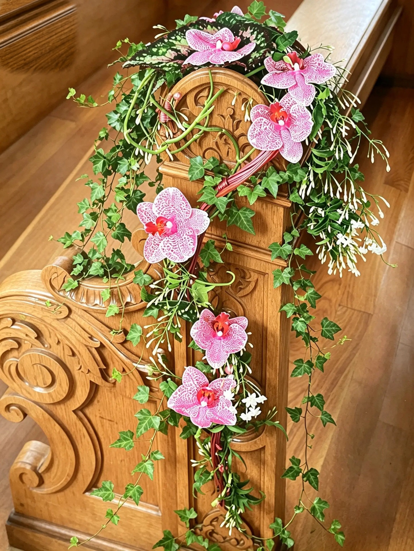Floraler Kirchenbankschmuck aus pinkfarbenen Orchideen, Efeu und geschwungenen Zweigen