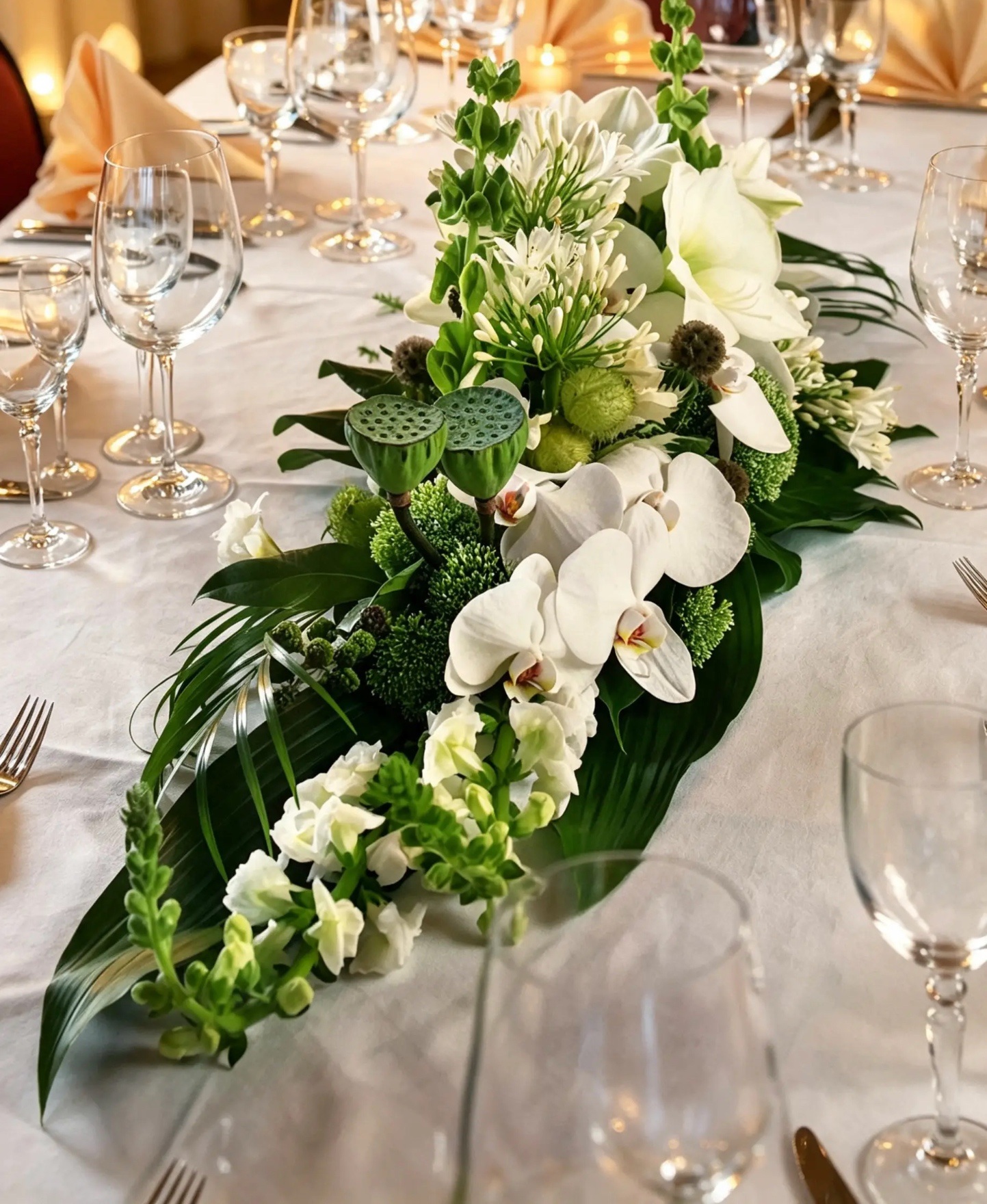 Längliches weiß-grünes Tischarrangement aus Orchideen, Lilien und Lotusfrüchten