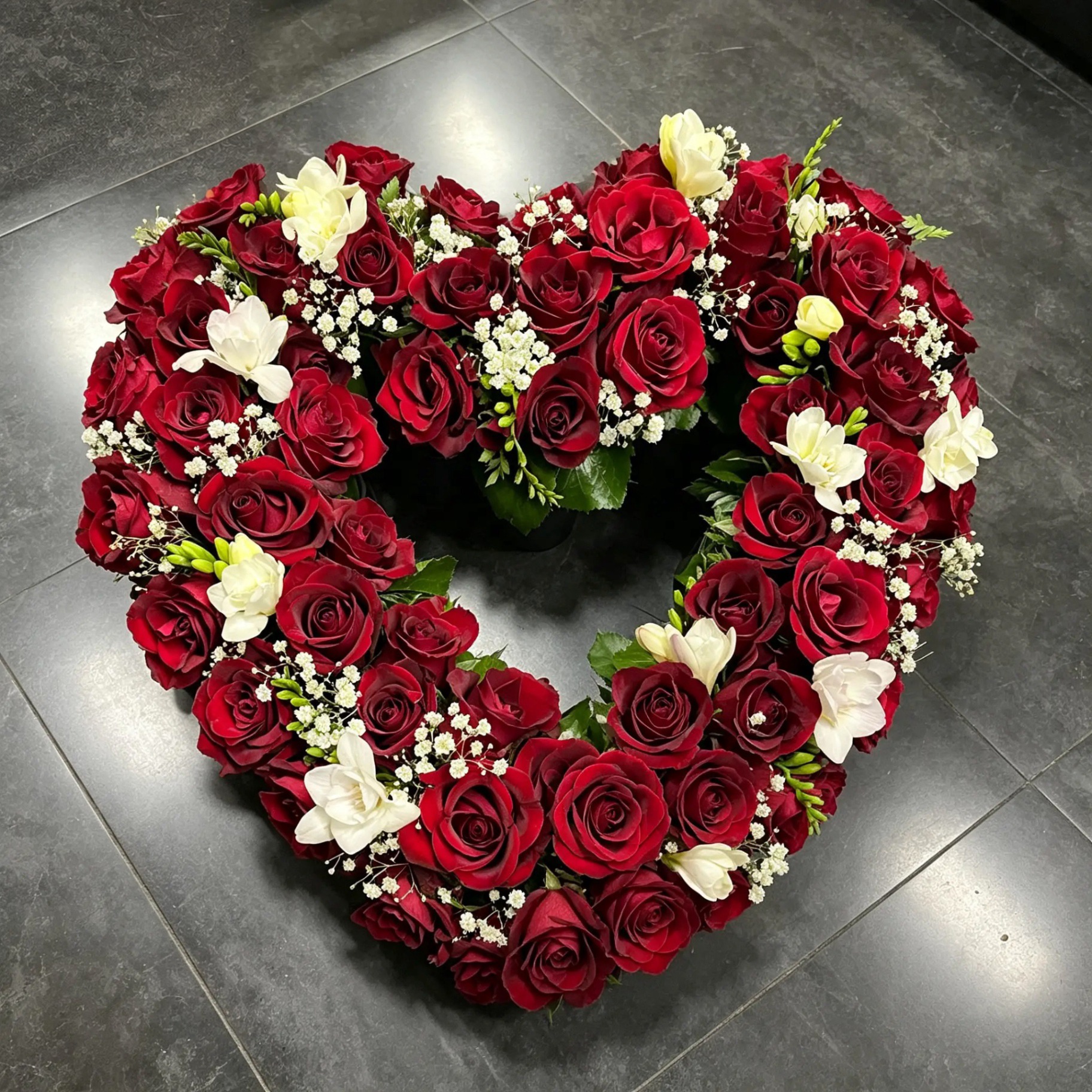 Herz aus rosa und lila Rosen mit beschrifteter Schleife