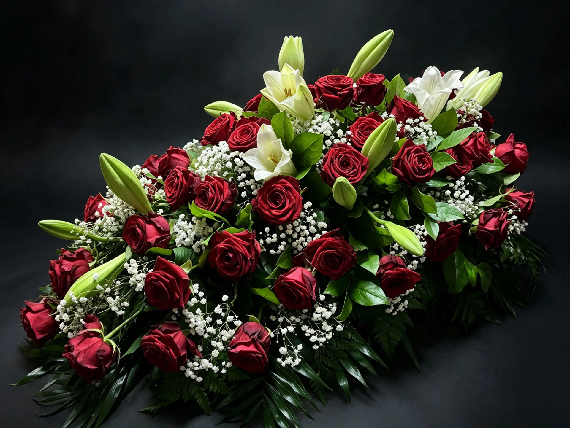 Trauergebinde aus dunkelroten Rosen, weißen Lilien und Schleierkraut