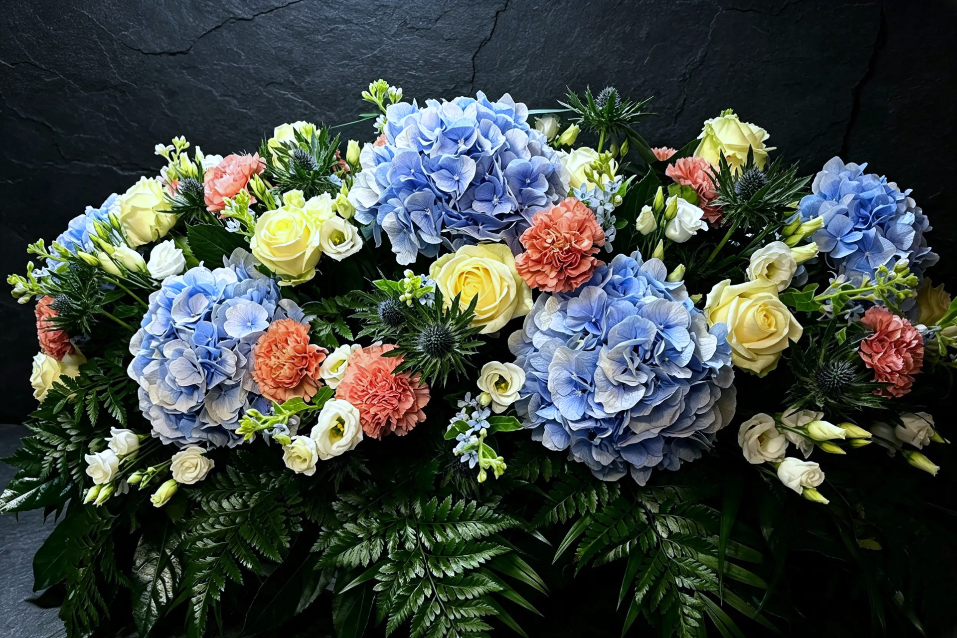 Trauergebinde mit blauen Hortensien, cremefarbenen Rosen und lachsfarbenen Nelken