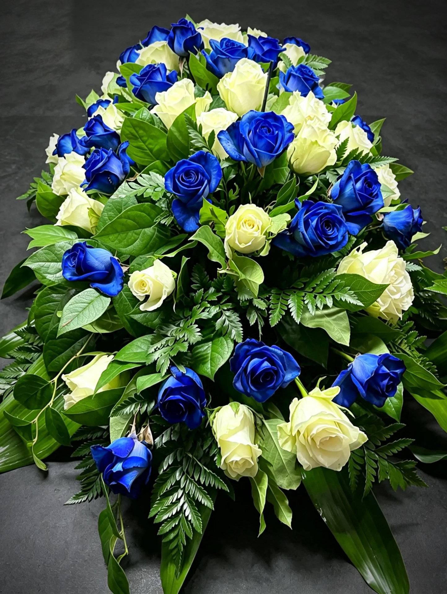 Trauergebinde aus tiefblauen und cremefarbenen Rosen mit Farn